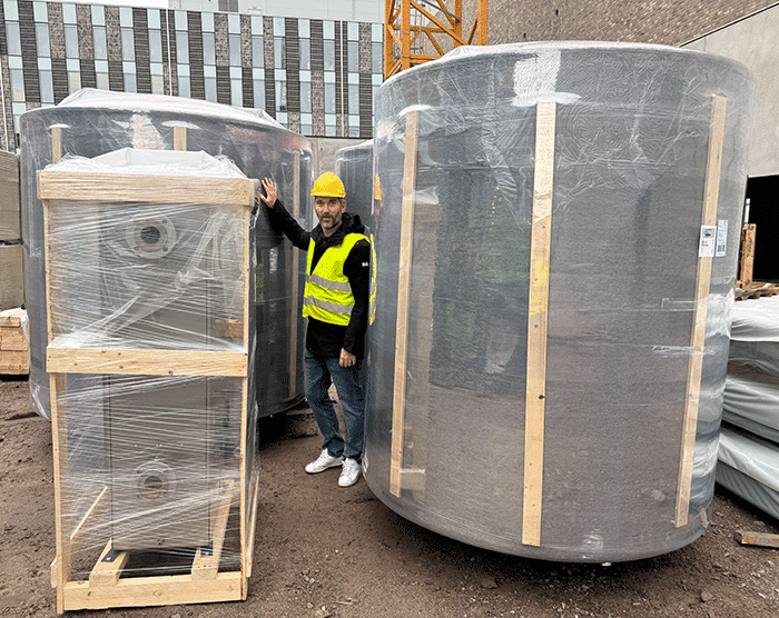 Person i skyddsväst och hjälm bredvid nyligen levererade ackumulatortankar på byggarbetsplatsen i Kalmar hamn.