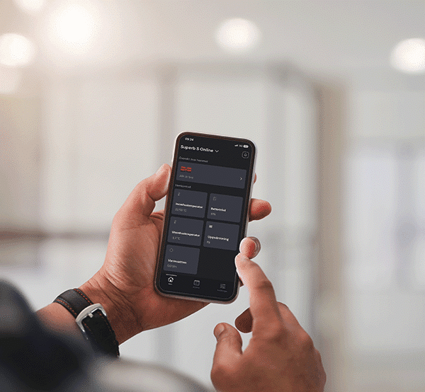 Hand som håller mobiltelefon med app för styrning av fjärrvärmecentral i fastighet